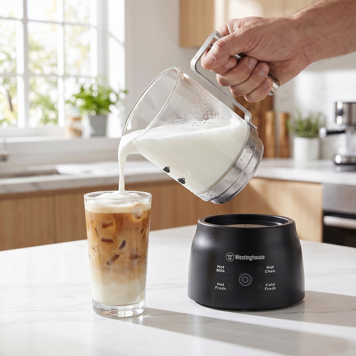 A hand pours milk from a clear pitcher into a glass of iced coffee above a black Westinghouse countertop hot/cold drink maker on a kitchen counter.